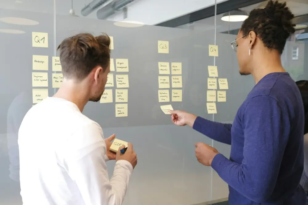 Two people collaborating on a project plan using yellow sticky notes on a glass wall, illustrating open-source governance